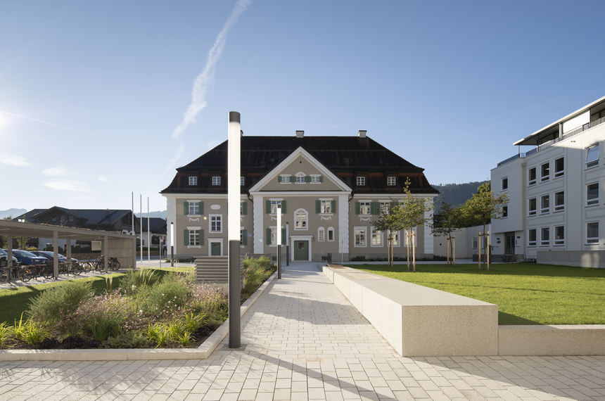 Landratsamt Garmisch-Partenkirchen, historisches Gebäude mit Stuckfassade, davor Freifläche mit Weg, Rasenfläche und Beleuchtung